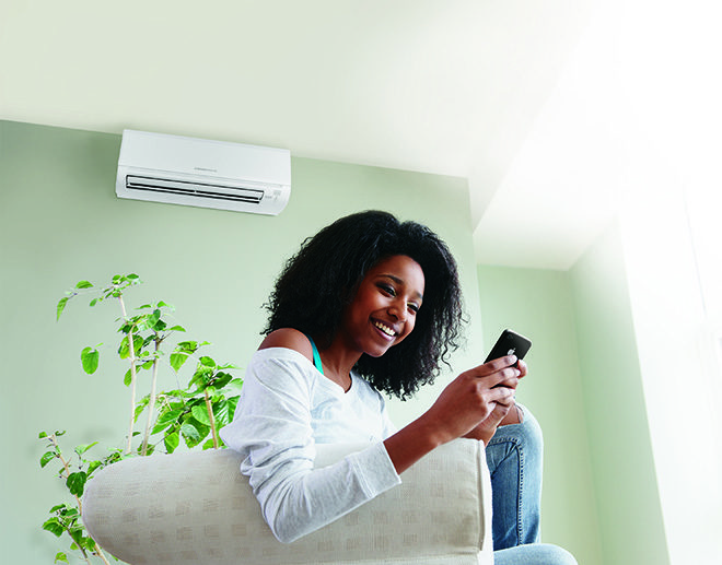 Woman using phone in comfort with Ductless Mini Split Unit on wall